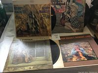 Photo of four vintage vinyl LP album covers and partially visible discs, showing titles and cover art.