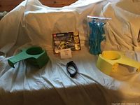 Various items on white fabric couch: Lego Creator 3-in-1 helicopter set, green and yellow plastic holders, USB cable.