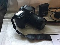 Close-up of camera body with attached lens, strap in foreground and charger behind