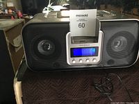 Front view of Insignia docking station showing speakers, digital display tuned to radio, and control buttons below the display.