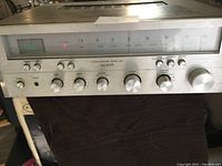 Front angle view of the Lloyds stereo receiver showing silver front panel, control knobs, AM/FM analog tuner dial, and indicator light on.