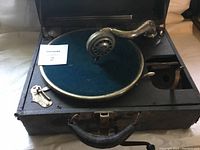 Antique phonograph with a hand crank and covered turntable, seen from the front and top angle