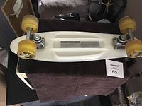 Bottom view of small white skateboard showing yellow wheels and metal trucks.