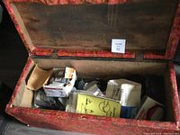 Overhead photo of open red wooden storage trunk filled with assorted boxes, bags, and manuals of plumbing supplies and hardware parts.
