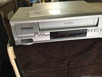 Front view of the white Sylvania video cassette player, showing cassette slot and control buttons on front panel.