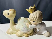 Photo of a Precious Moments ceramic figurine showing a child in white with a gold crown hugging a camel covered with a green polka dot blanket.