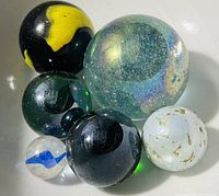 Photo showing six assorted collectible marbles of various sizes, colors, and patterns.