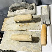 Four assorted mason trowels laid out on a light surface, showing different blade shapes and handle materials.
