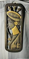 Front view of the wooden carved wall art showing a woman in profile with hat, earrings, neck rings, and intricate design details in dark brown and golden accents.