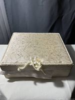 Closed view of fabric-covered keepsake box with decorative scroll pattern and rope-style button closure.
