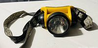 Front view of yellow Energizer head gear light showing single central bulb with black casing and attached adjustable fabric straps.