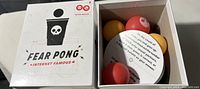 Top-down view of Fear Pong game box containing three colored balls and several round instruction cards inside