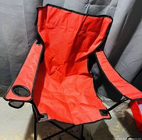Front view of the red folding camping chair, showing fabric seat, armrests, and mesh cup holder on the right side.