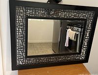 Rectangular wall mirror with black metal frame featuring geometric cutout design. The mirror surface is clean and reflective.