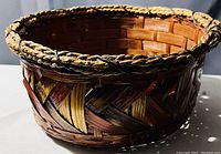 Close-up photo of round woven basket showing color pattern and braided rim detail.