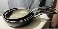 Set of three stone-look frying pans with stainless steel handles nested by size