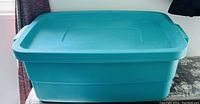 Photo showing a large turquoise plastic storage tote with its lid on, in good condition.