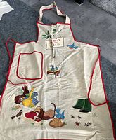 Photo showing vintage barbecue apron laid flat on a floor with colorful illustrations and red trim.