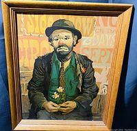 Frontal photo of framed clown wall art showing a sad clown holding daisies with a mixed text background.