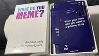 Top-down photo of the What Do You Meme? game box with cards inside showing sample cards with meme captions.