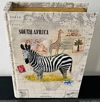 Shows rectangular fabric-covered keepsake box designed like a book with zebra and African animals on cover and African map background.