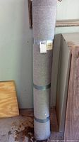 Full view of rolled area rug secured with two gray straps standing upright.