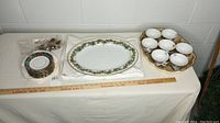 Full lot from left to right showing stacked saucers, oval platter with floral border, and scalloped tray holding seven cups.