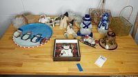 Full lot of Christmas items on wood table showing snowman figurines, decorative wire baskets with beads, round penguin plate, and framed snowman print.