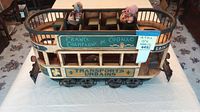 Front and side view of the wooden trolley showing exterior painted signage and dolls inside.