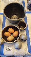 Top view showing large pottery bowl with spout, smaller bowl with eggs, small cup, and two ceramic decorative eggs painted with cows and sheep.