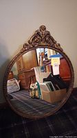 Front view of round mirror with gold decorative frame showing reflection of room and lot sticker