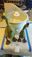 Photo showing front view of two green wooden duck figurines placed in front of the white West Bend crockpot on a table.