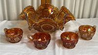 Full view of the large ruffled amber carnival glass bowl with four matching cups arranged in front.