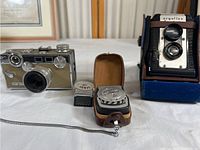 Front view of Argus C3 camera, Argoflex twin lens reflex camera in blue case, and two vintage light meters, one in brown leather case