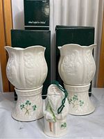 Front view of two Belleek fine Parian china hurricane lamps with woven basket bases and shamrock decoration, plus the Santa figurine in front