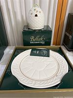 Image showing the Belleek honeypot placed on top of a green box labeled 'Belleek Fine Parian China', with the white decorative plate displayed in the box below it.