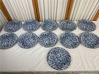 Full set of 11 blue and white floral plates displayed on a table, all uniform design and size.