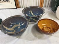 Photo of three pottery bowls on white cloth, two are blue with cream glaze, one is brown glazed bowl
