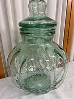 Front view of light green pumpkin-shaped glass jar with lid on top, showing distinctive pumpkin segment ridges and ribbed ring design on lid.