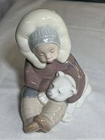Front view of Lladro porcelain figurine showing Inuit child embracing polar bear pup.