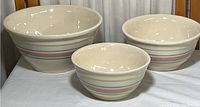 Three nested vintage McCoy pottery ovenware bowls in cream with pink and blue stripes.