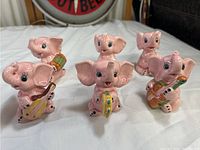 Front view of all five pink elephant musician band figurines arranged in a semi-circle on white fabric, showing each elephant holding a different musical instrument.