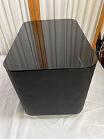 Glossy black wireless subwoofer unit with minor dust and reflections of window on its top surface.