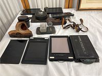 Vintage film equipment with three black Risography 55 film holders, leather cases and straps, film canister and small accessories