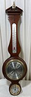 Full view of the vintage wooden Howard Miller barometer showing the thermometer, barometer dial, and hygrometer.