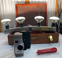 Sears Roebuck light tower with four bulbs mounted on a horizontal metal bar, mounted on wooden base case; Revere camera and red winding tool in front