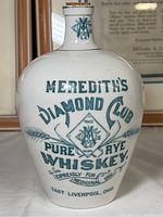 Front view of ceramic whiskey decanter with Meredith's Diamond Club branding in green lettering.