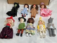 Photo showing all nine dolls arranged in two rows on a white surface with a cardboard box in the background.