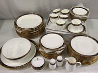 Photo showing full set of plates, cups, saucers, plus creamer, salt and pepper shakers, covered sugar bowl, and serving bowl and platter, all featuring the Mikasa Cagii Royal Glimmer pattern with gold trim and geometric borders.