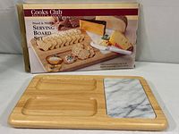 Photo showing Cooks Club Wood & Marble Serving Board Set in original packaging with the board placed in front of the box which depicts the product use with crackers, cheese, and condiments.